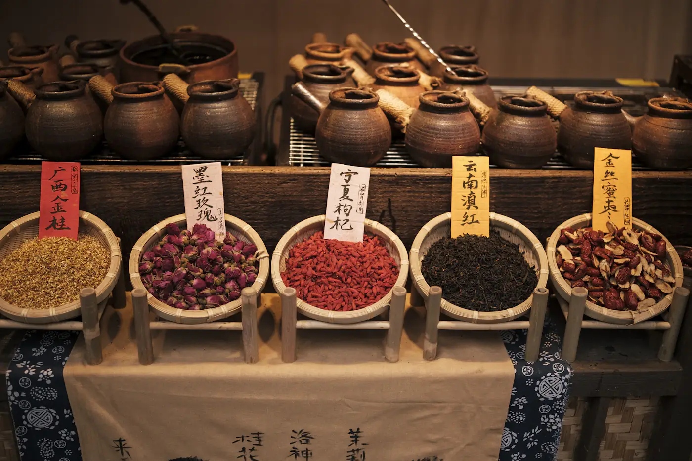 Chinese herbal pharmacy counter with clay jars and bowls of labeled dried herbs, goji berries and roots